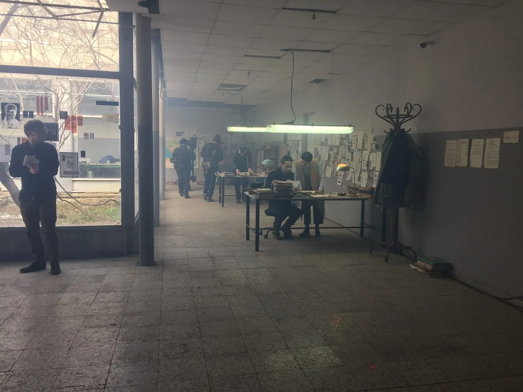 Actors and crew on the newsroom set in a long, half-empty studio hall.