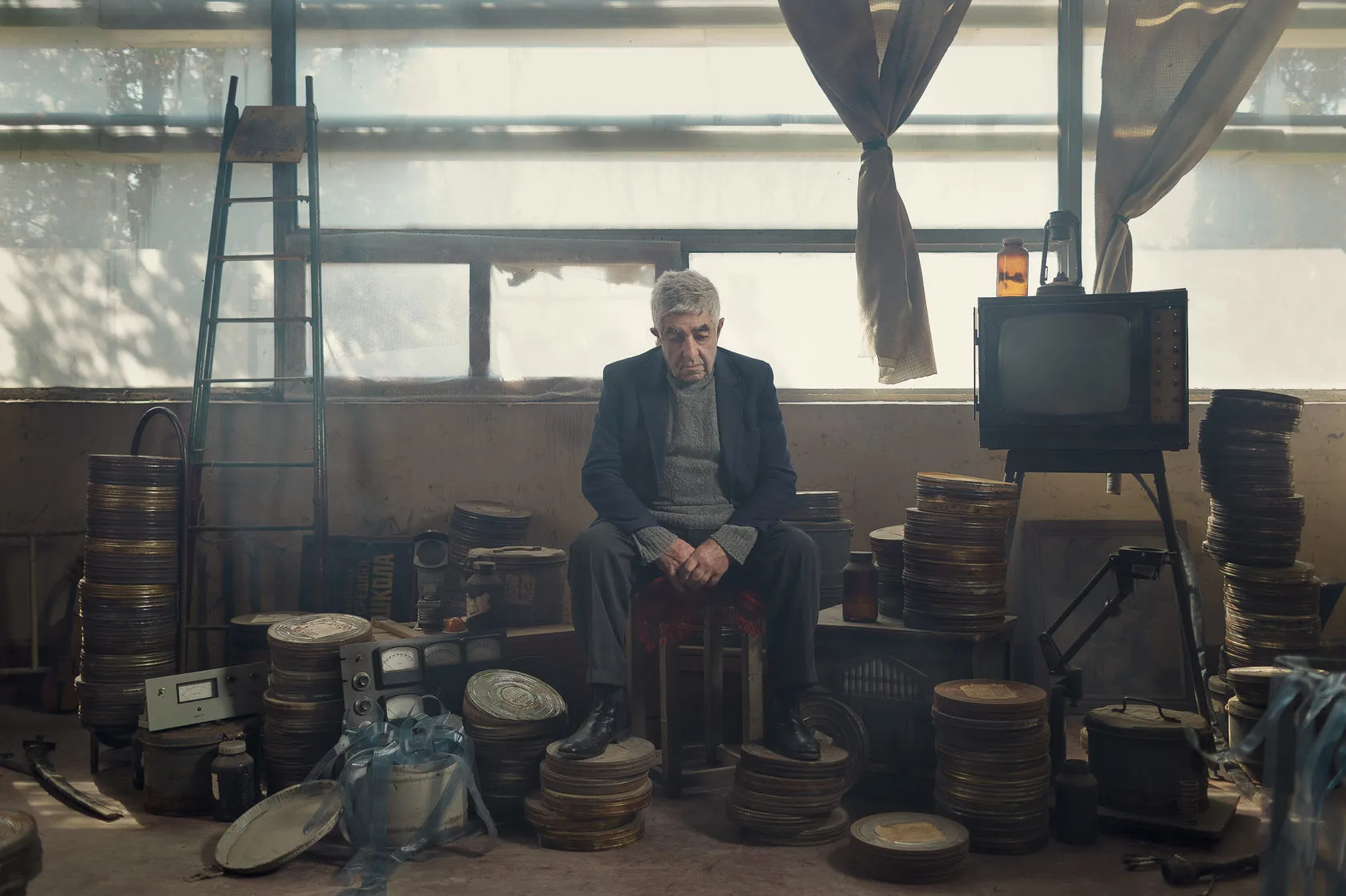 Robert sits among stacks of film cans, an old television beside him.