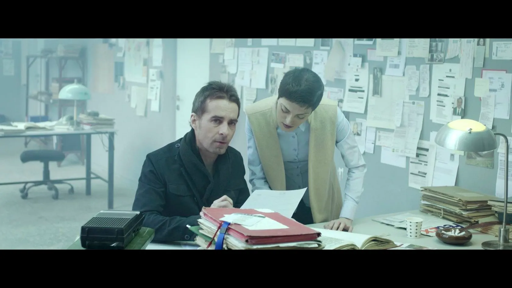 n_vestigate by Andrei Kovalev: two investigators study photographs and notes pinned above a cluttered desk.