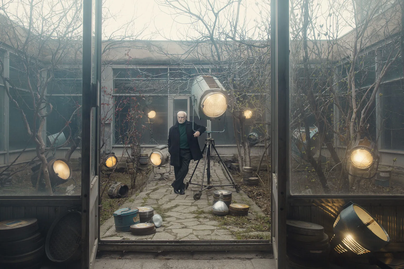 Batoni Merab leans on a large film light in a glass courtyard among old lamps and film cans.