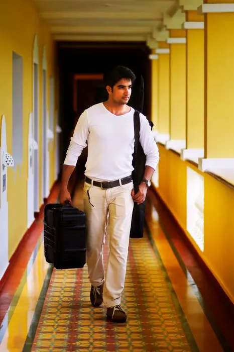 A man in white walks down a yellow colonnaded corridor, carrying a black case.