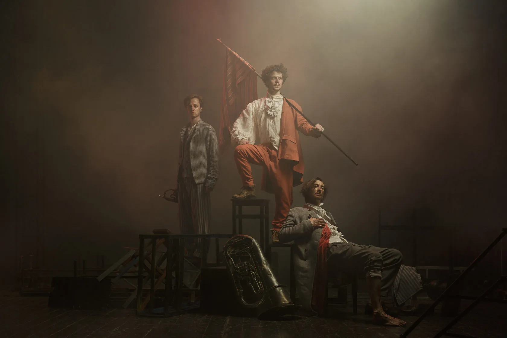Three actors in French Revolution costume pose on a smoky stage, one raising a red striped flag.