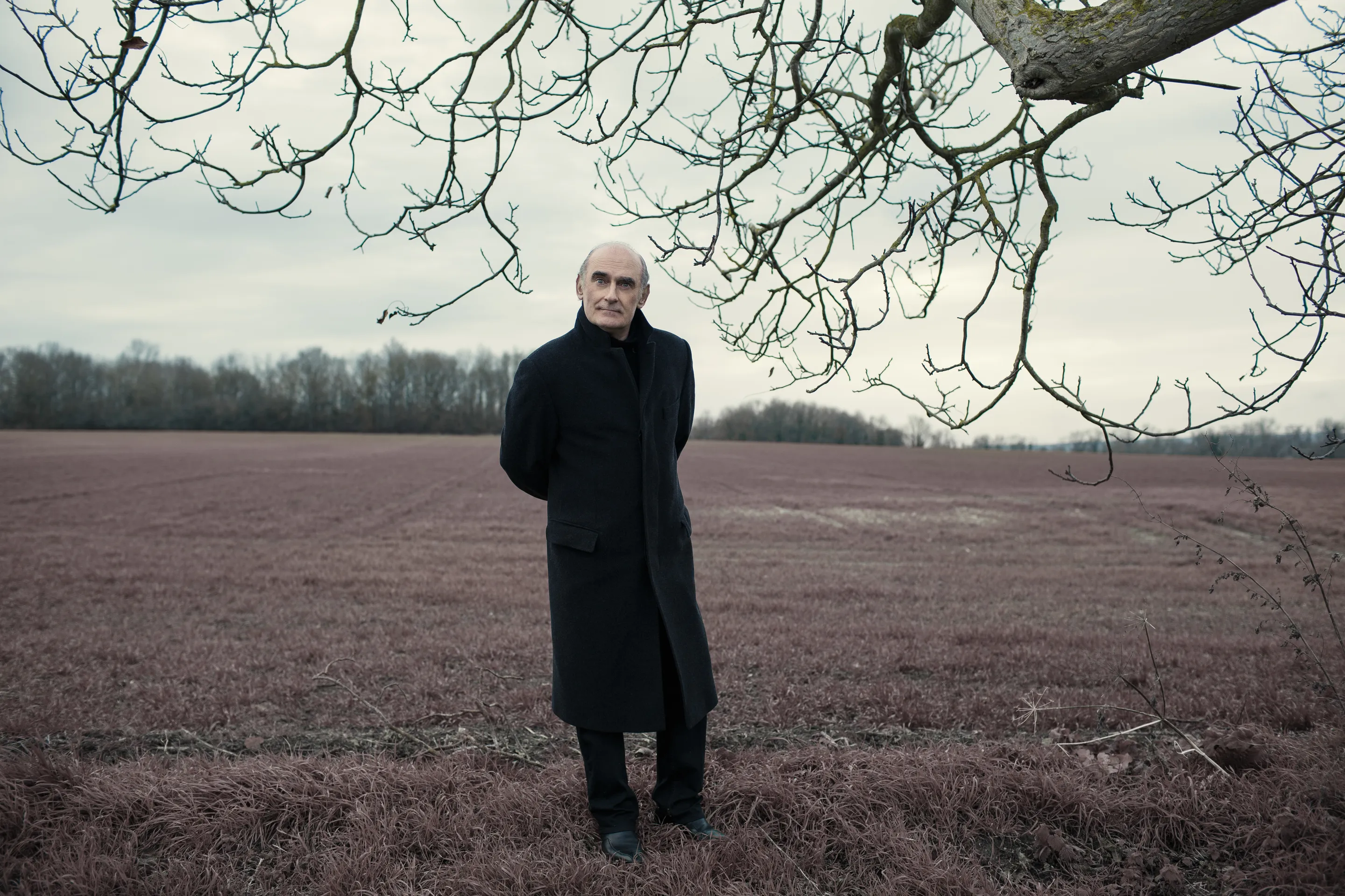 Michel Honaker press portfolio by Andrei Kovalev: a man stands in an open field beneath bare winter branches.