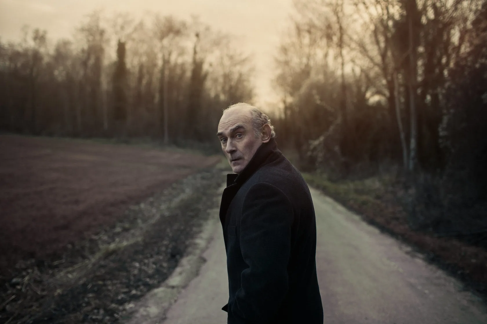 Michel looks back over his shoulder on a country road at dusk.