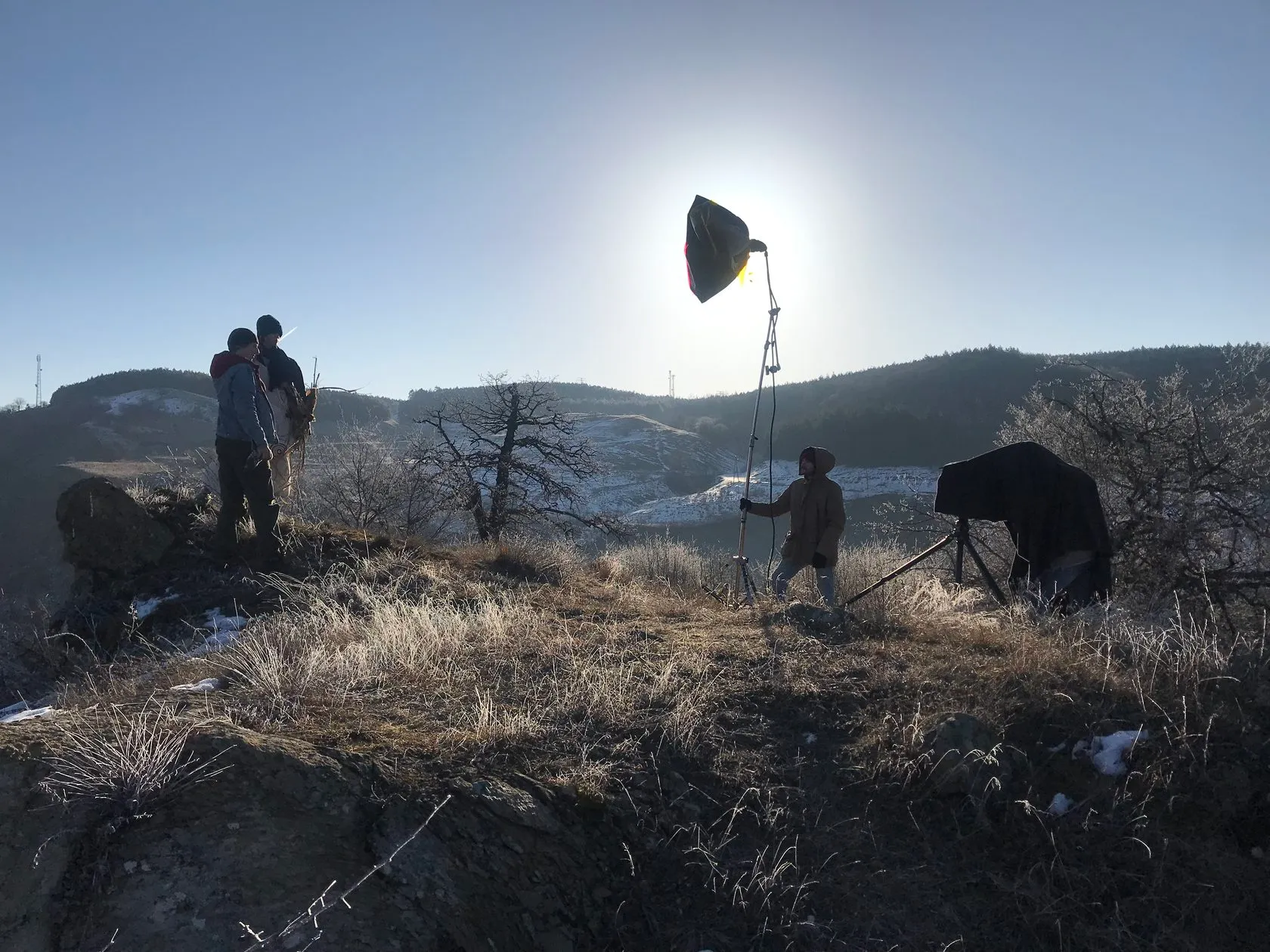 A crew sets up a large-format camera and a softbox on a frosty hilltop.