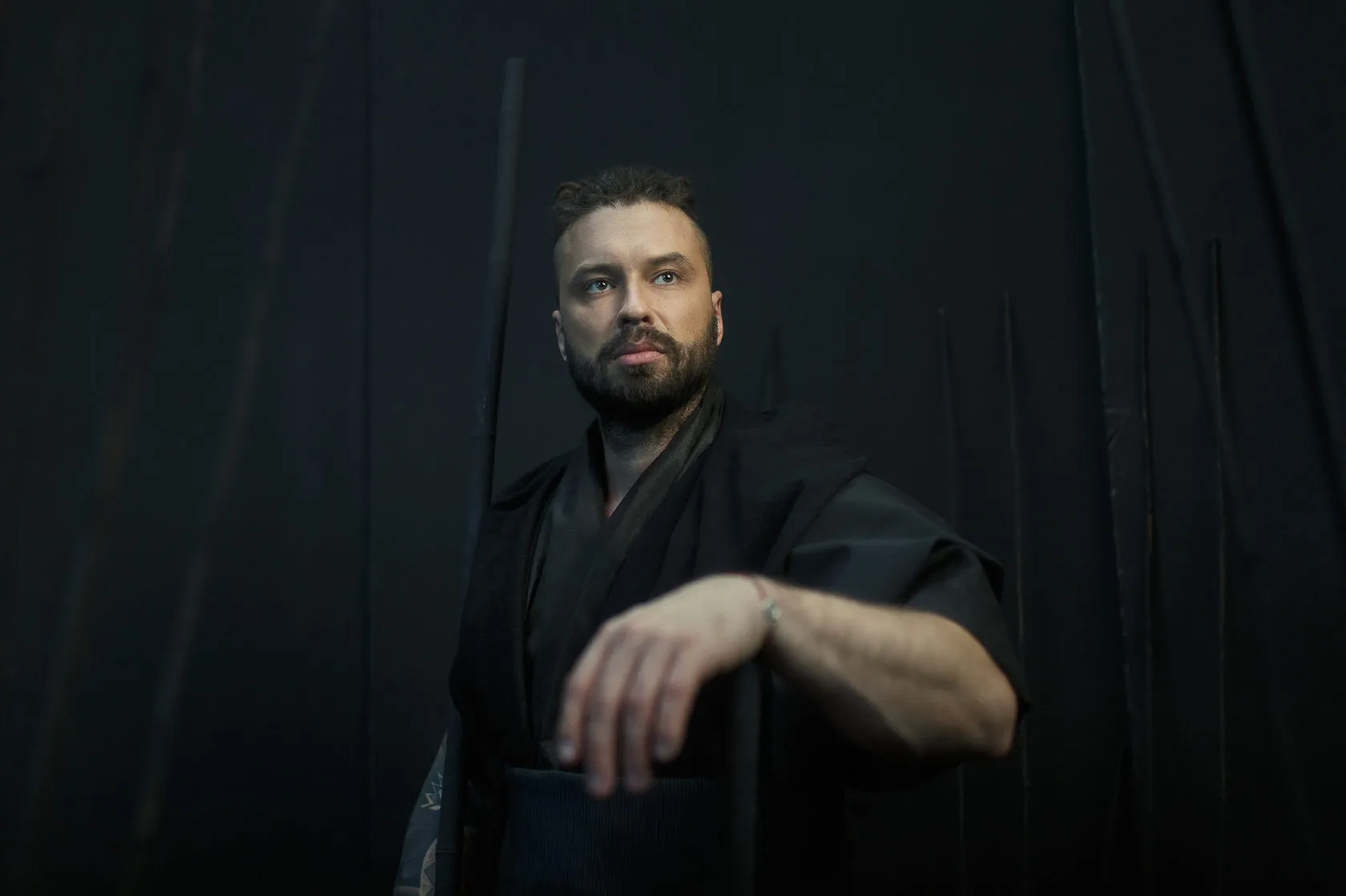 A bearded Burito musician in a black kimono rests his forearm on a ledge.