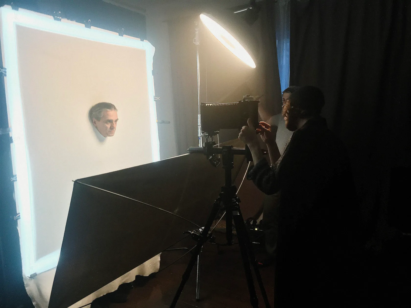 An actor’s head through a hole in a lit white sheet, photographed on a large-format camera.