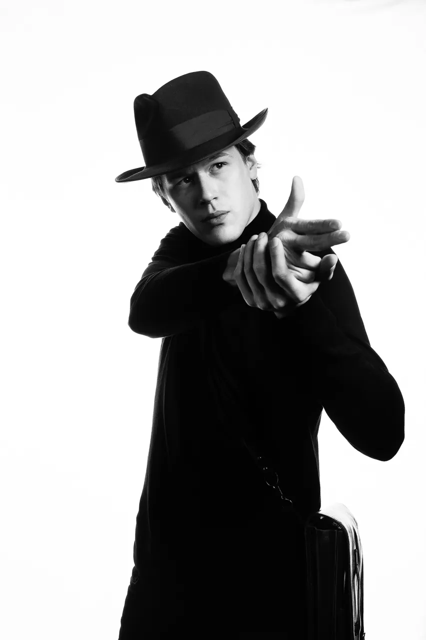 An actor in a fedora points at the camera.