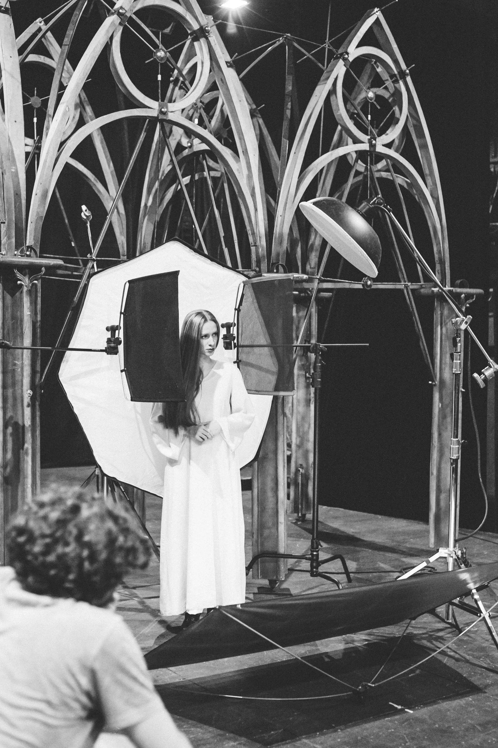 Behind the scenes: an actress in a long white gown stands in front of the light.